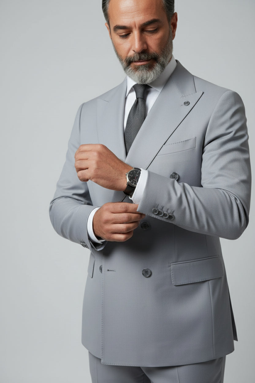 Man adjusting cuff of light grey double-breasted suit with peak lapels.
