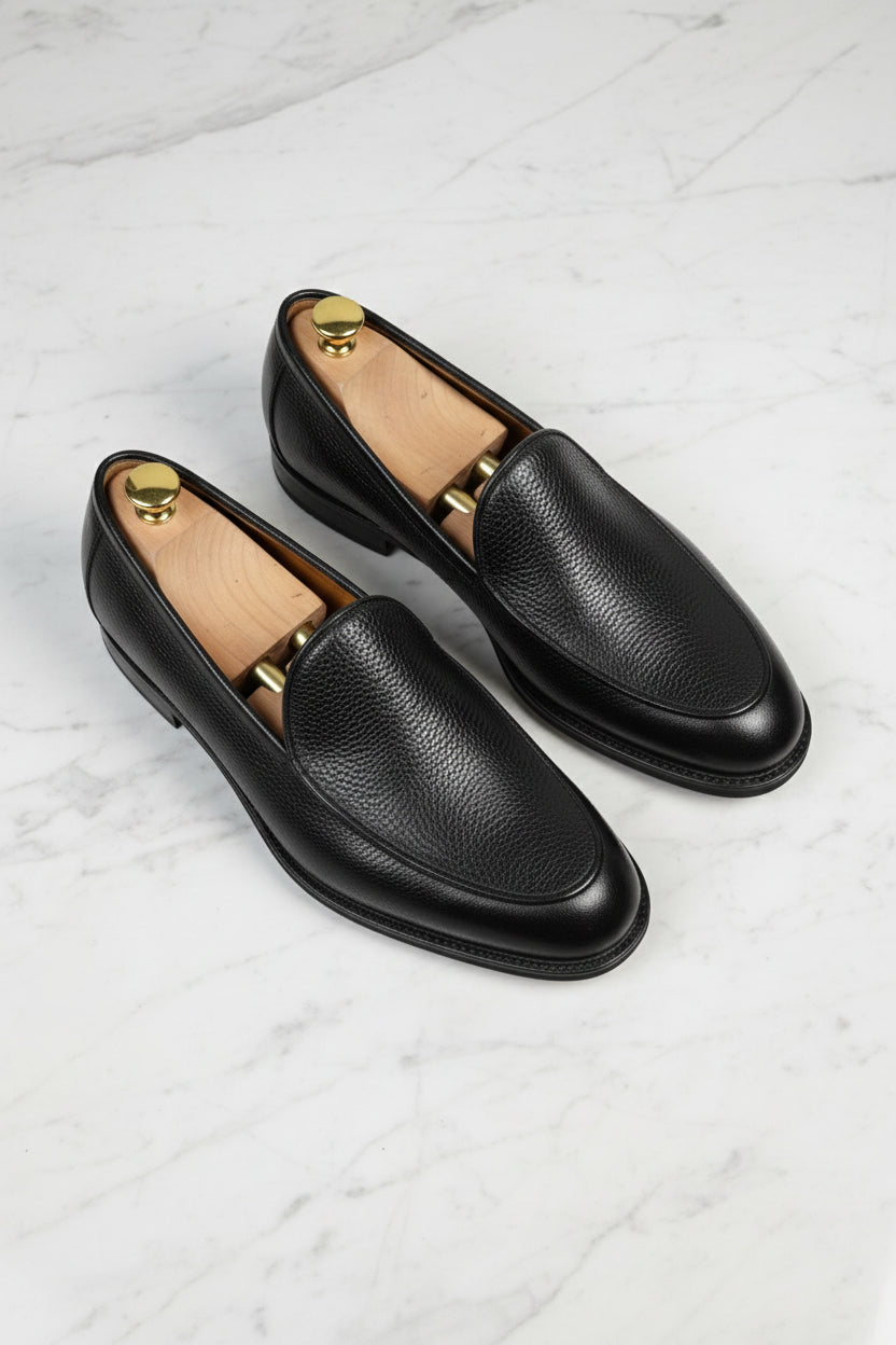 Black leather slip-on loafers with textured finish, ideal for formal and casual wear.