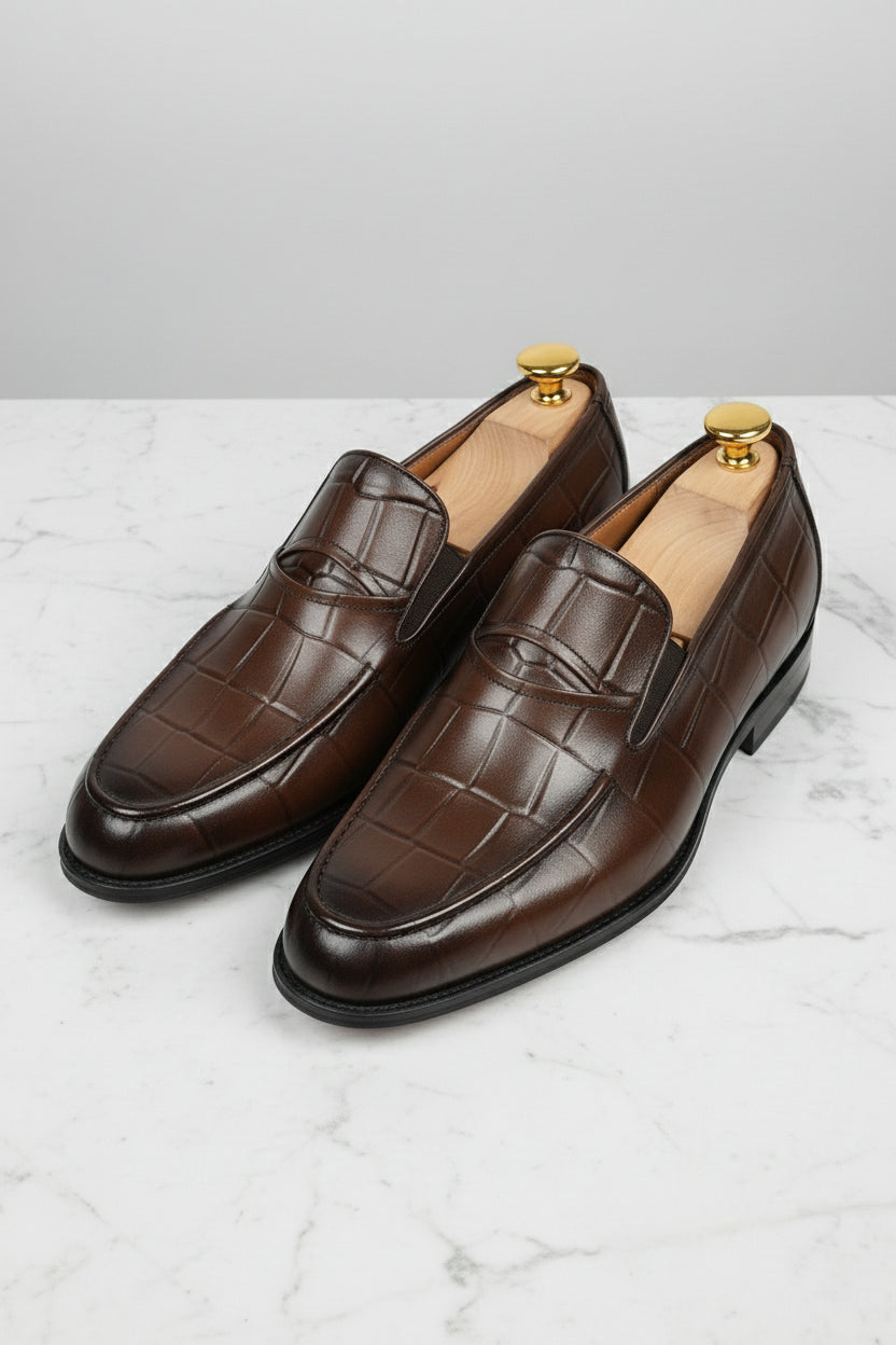 Brown crocodile-embossed slip-on shoes with elegant leather finish for formal wear.