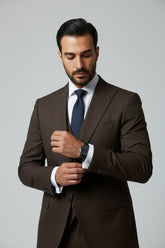 Man adjusting cuff of brown slim fit three-piece suit with elegant watch.