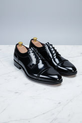 Black patent leather dress shoes with lace-up design and elegant cap-toe detail.