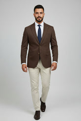 Man in brown and beige slim-fit two-piece suit with navy tie and dress shoes.