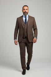 Man in brown three-piece suit with tailored fit and blue shirt, walking confidently.