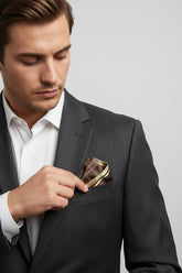 Man adjusting brown silk pocket square with plaid design in suit jacket pocket.