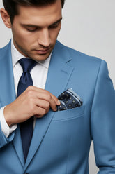 Man adjusting navy geometric silk pocket square in light blue suit jacket.