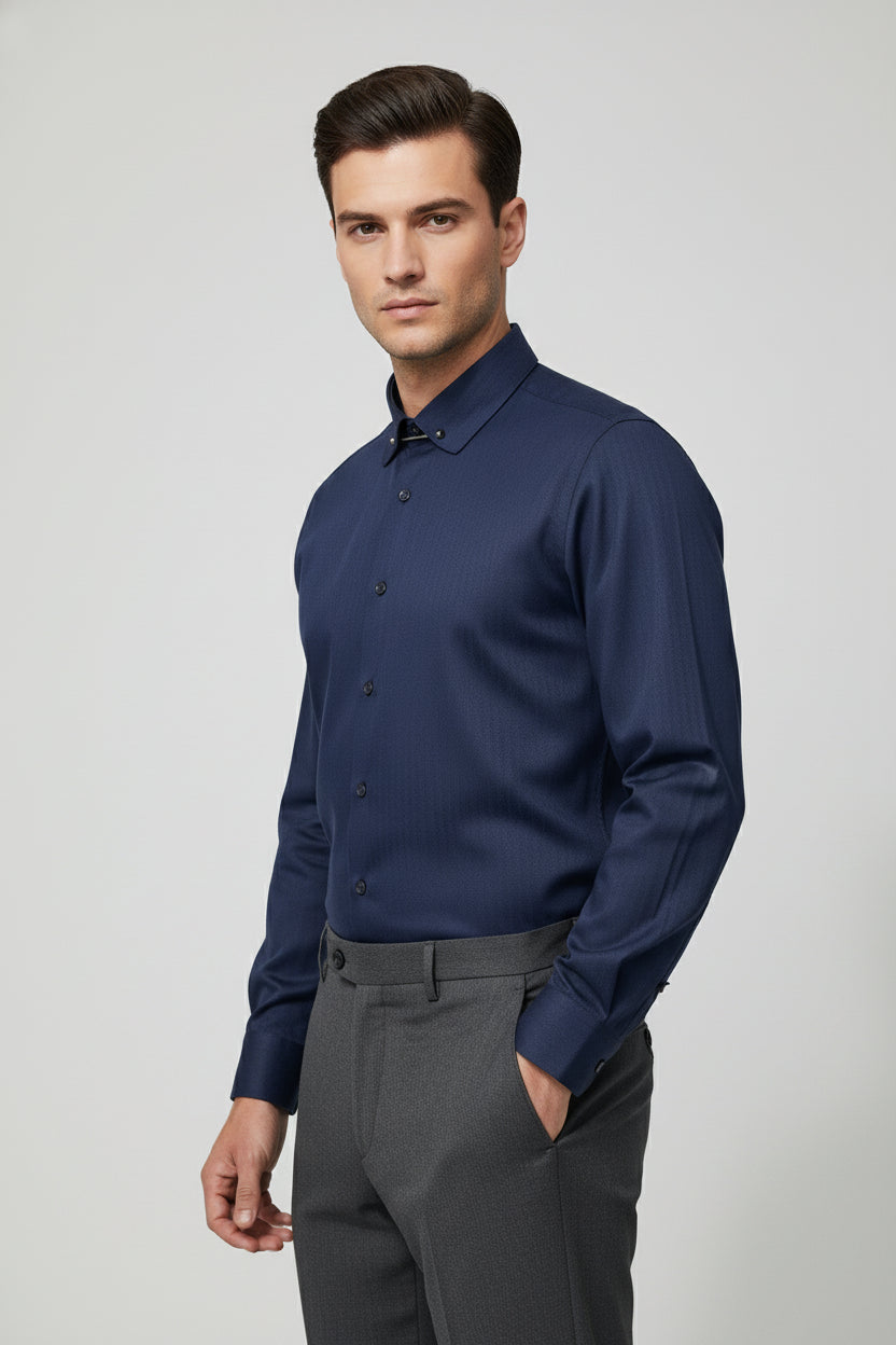 Man wearing navy herringbone dress shirt with collar bar and tailored grey trousers.