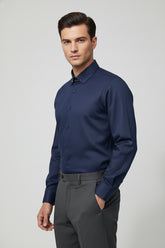 Man wearing navy herringbone dress shirt with collar bar and tailored grey trousers.