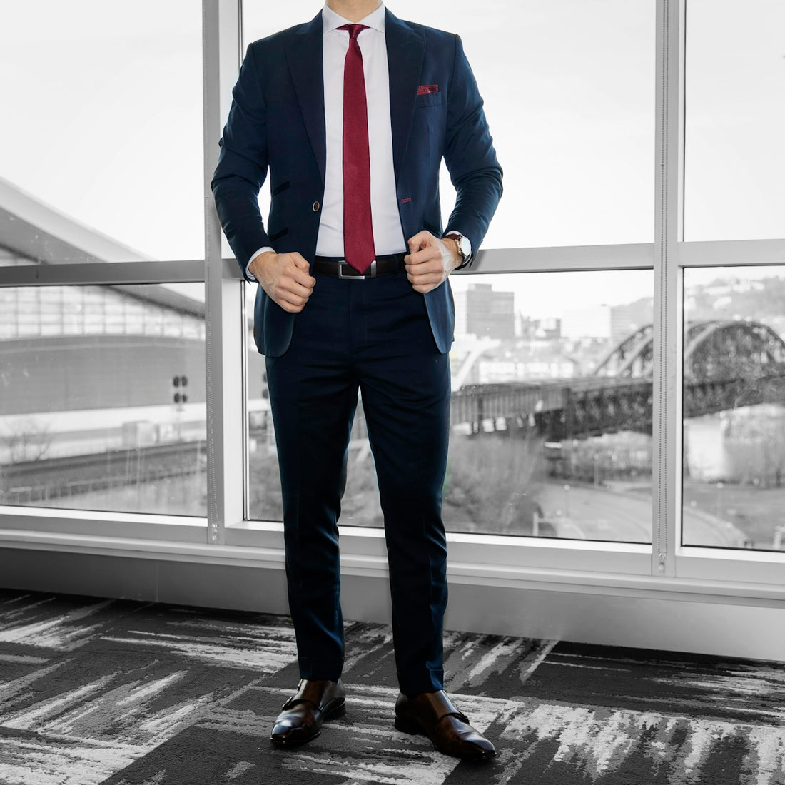 man in blue dress shirt and blue denim jeans standing near glass window