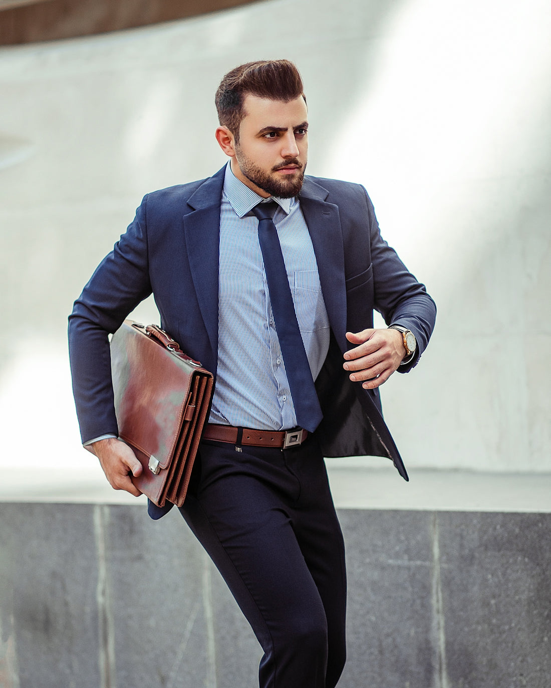 man in blue suit jacket and black pants holding brown leather bag