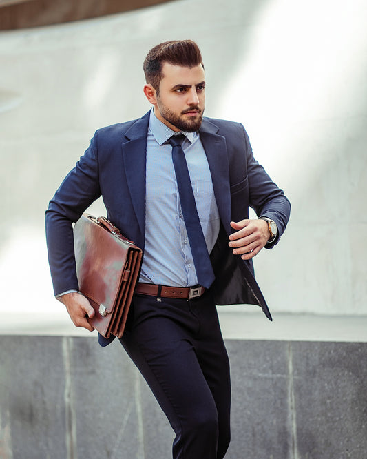 man in blue suit jacket and black pants holding brown leather bag