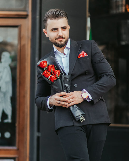 man in black suit holding red rose bouquet