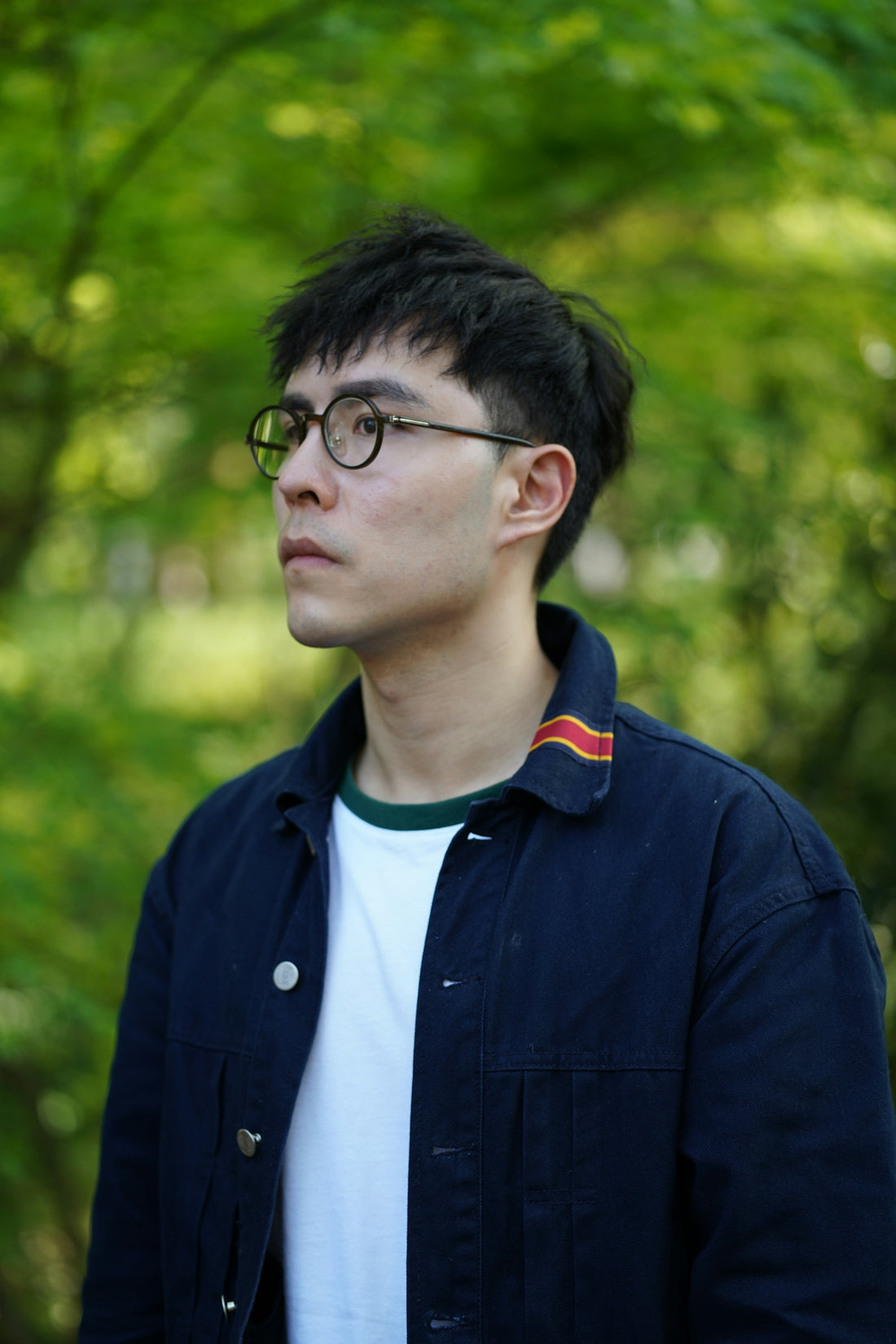 a man with glasses standing in front of trees