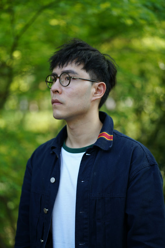 a man with glasses standing in front of trees