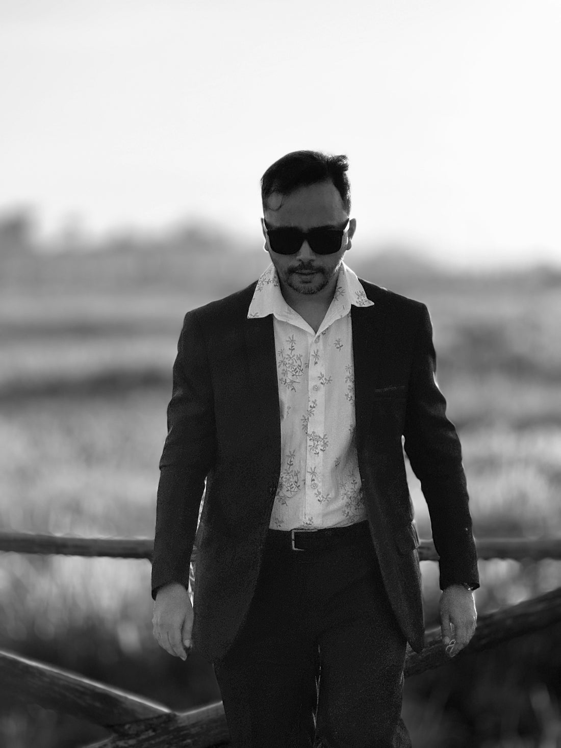a man in a suit and sunglasses walking across a bridge