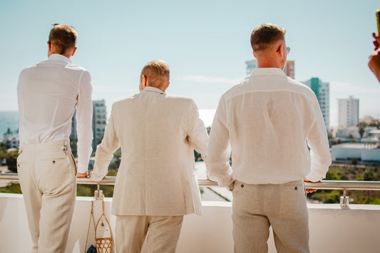 Three men in white suits on a balcony overlooking city.