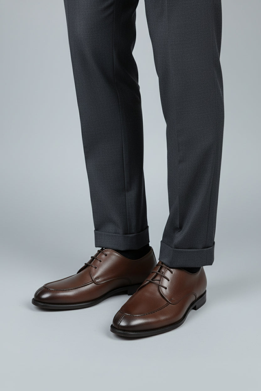 Brown leather lace-up dress shoes paired with grey tailored trousers for formal occasions.