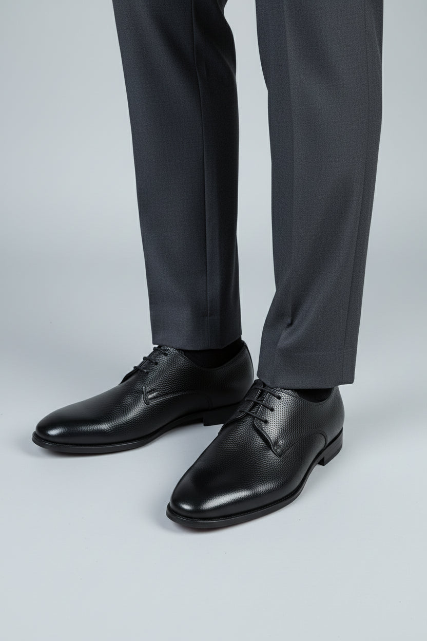 Black leather lace-up dress shoes paired with tailored grey trousers for formal occasions.