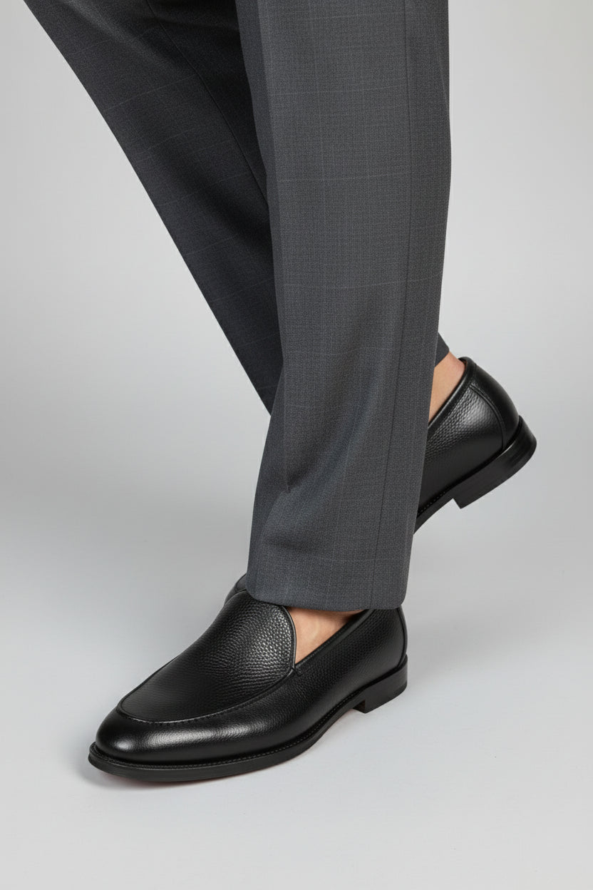 Man wearing black leather slip-on loafers with textured finish and formal trousers.