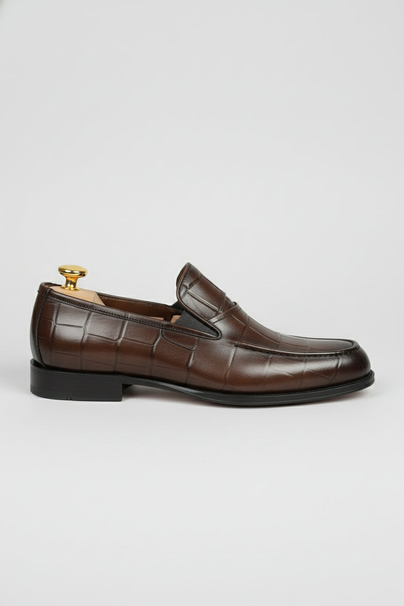 Brown crocodile-embossed slip-on shoes with elegant leather finish for formal wear.