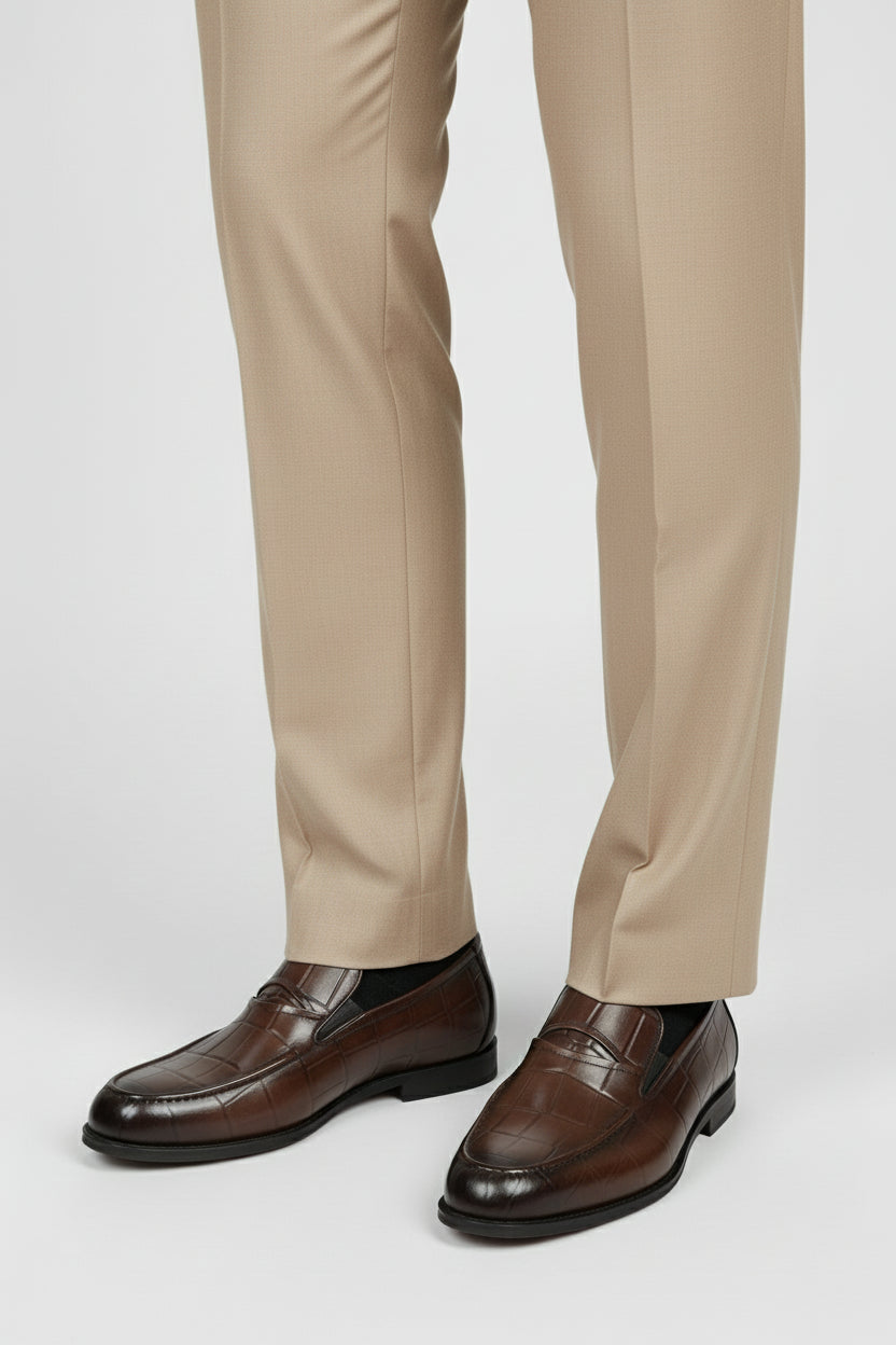 Brown crocodile-embossed slip-on shoes paired with beige formal trousers.