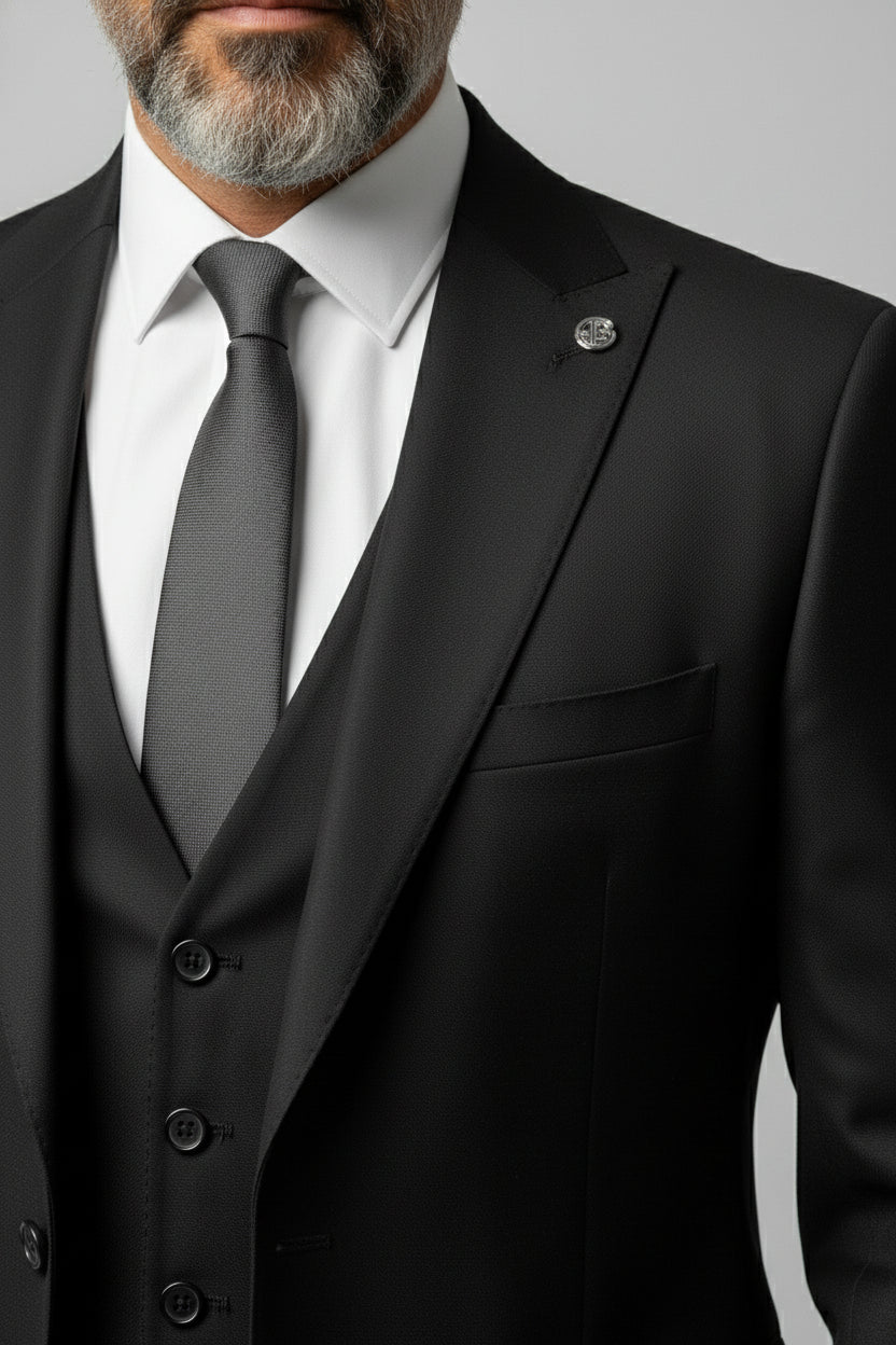 Man wearing black peak lapel three-piece suit with tailored fit and grey tie.