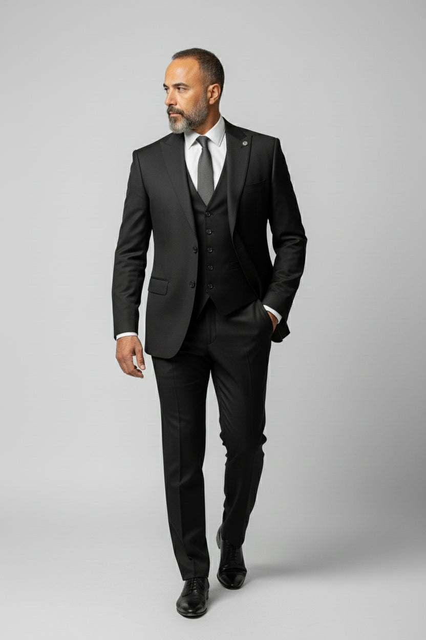 Man in black peak lapel three-piece suit with tailored fit, ideal for weddings or corporate events.