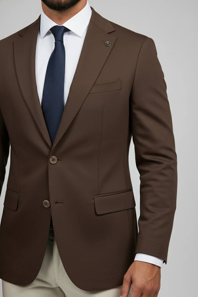 Man wearing a brown slim-fit suit jacket with beige trousers and a navy tie.