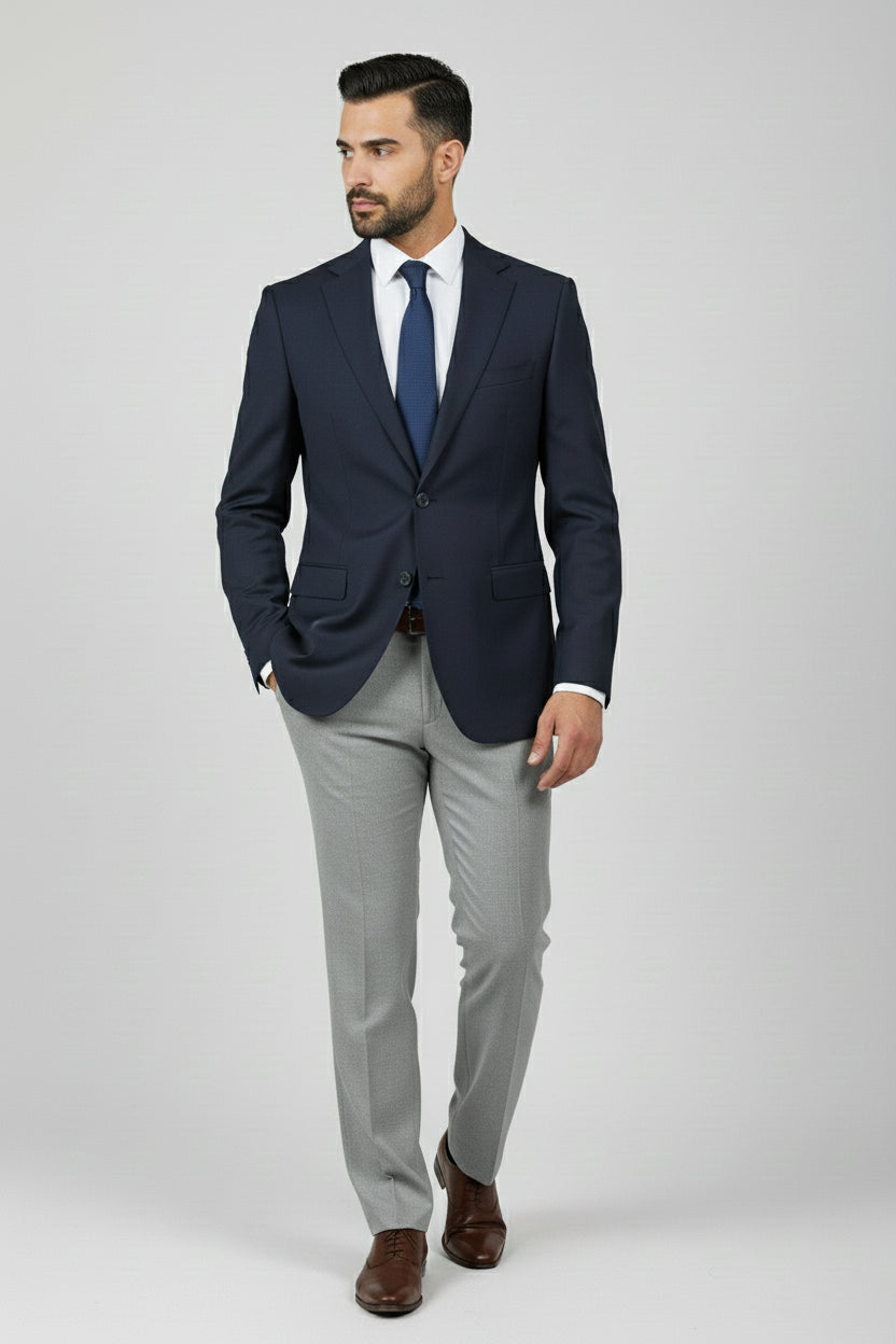Man in navy slim fit two-button suit paired with grey trousers and brown shoes.
