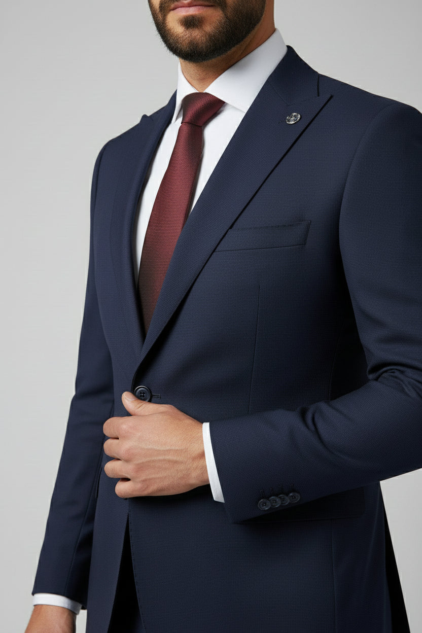 Man in navy two-piece slim fit suit with peak lapel and burgundy tie.