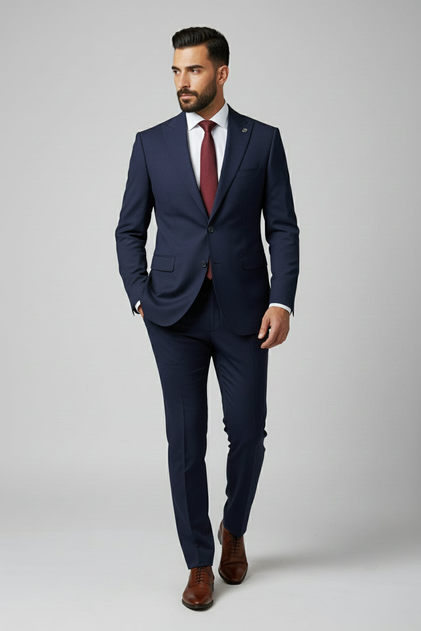 Man wearing navy slim-fit two-piece suit with peak lapels and burgundy tie.