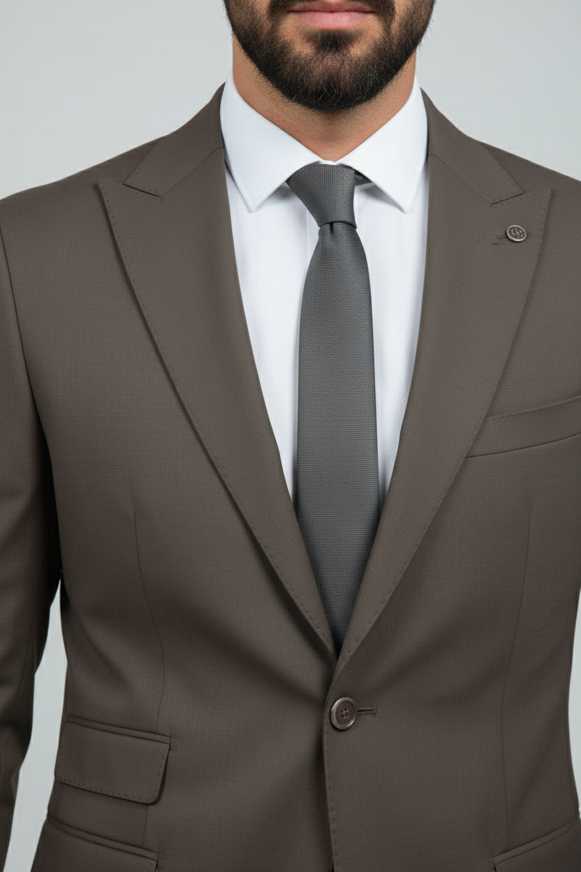 Man wearing brown three-piece suit with waistcoat and grey tie, tailored fit.