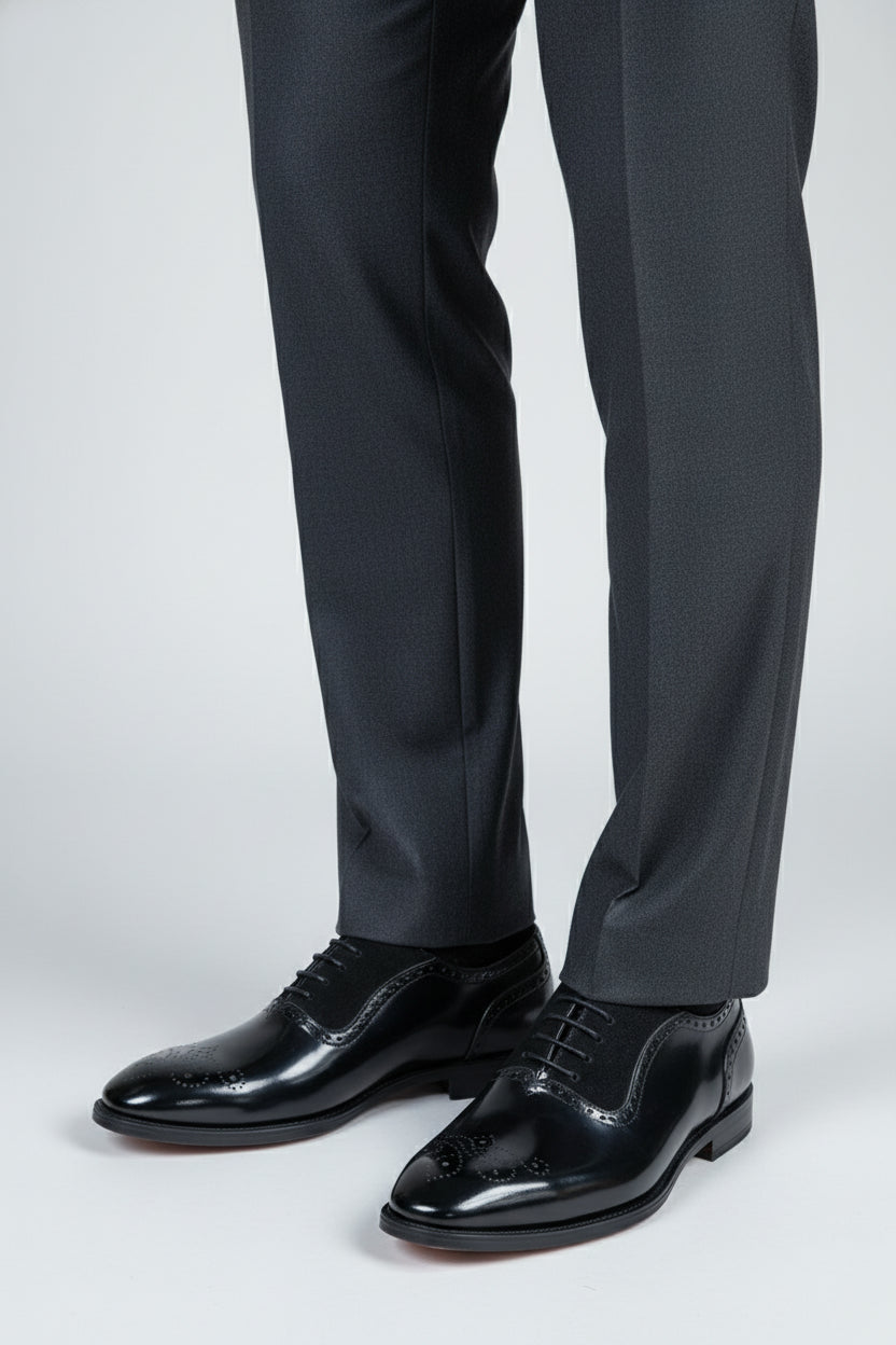 Black brogue Oxford shoes with contrast lining, paired with elegant grey trousers.