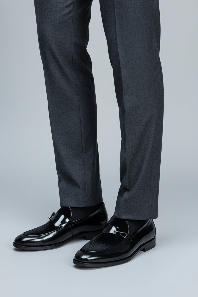 Black velvet loafers with elegant buckle paired with tailored grey trousers.