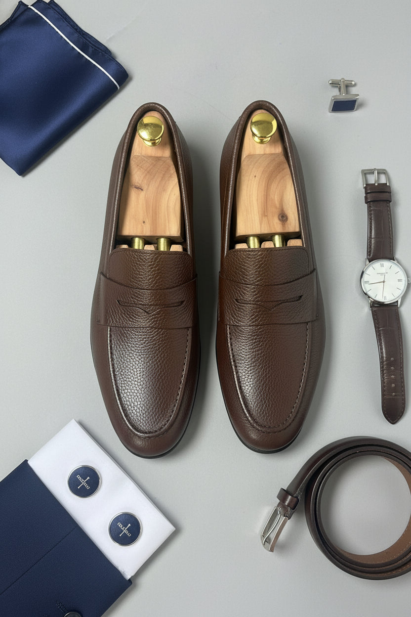 Dark brown leather slip-on loafers styled with wooden shoe trees and accessories.