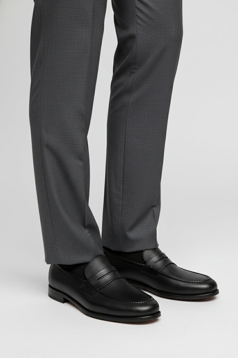 Black textured leather slip-on loafer paired with grey tailored trousers.