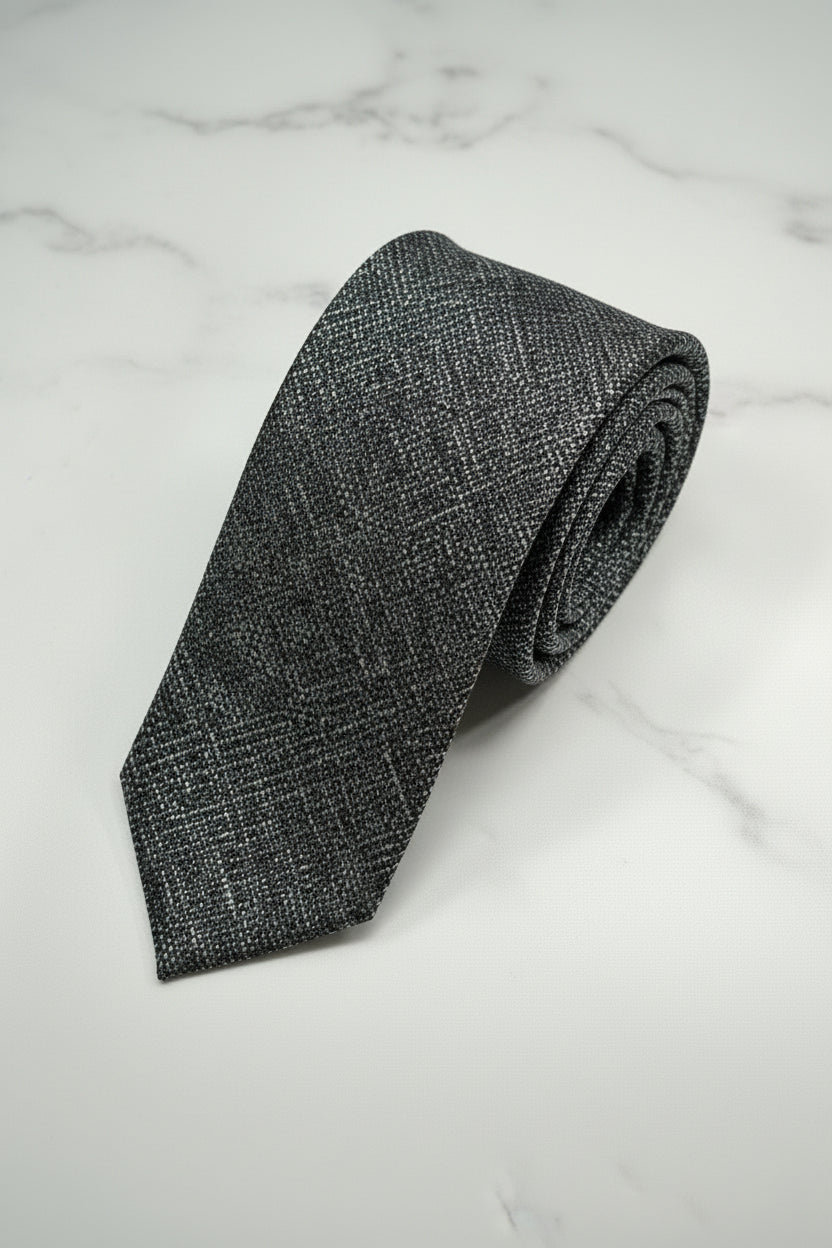 Navy textured silk tie rolled on a marble surface, ideal for formal wear.