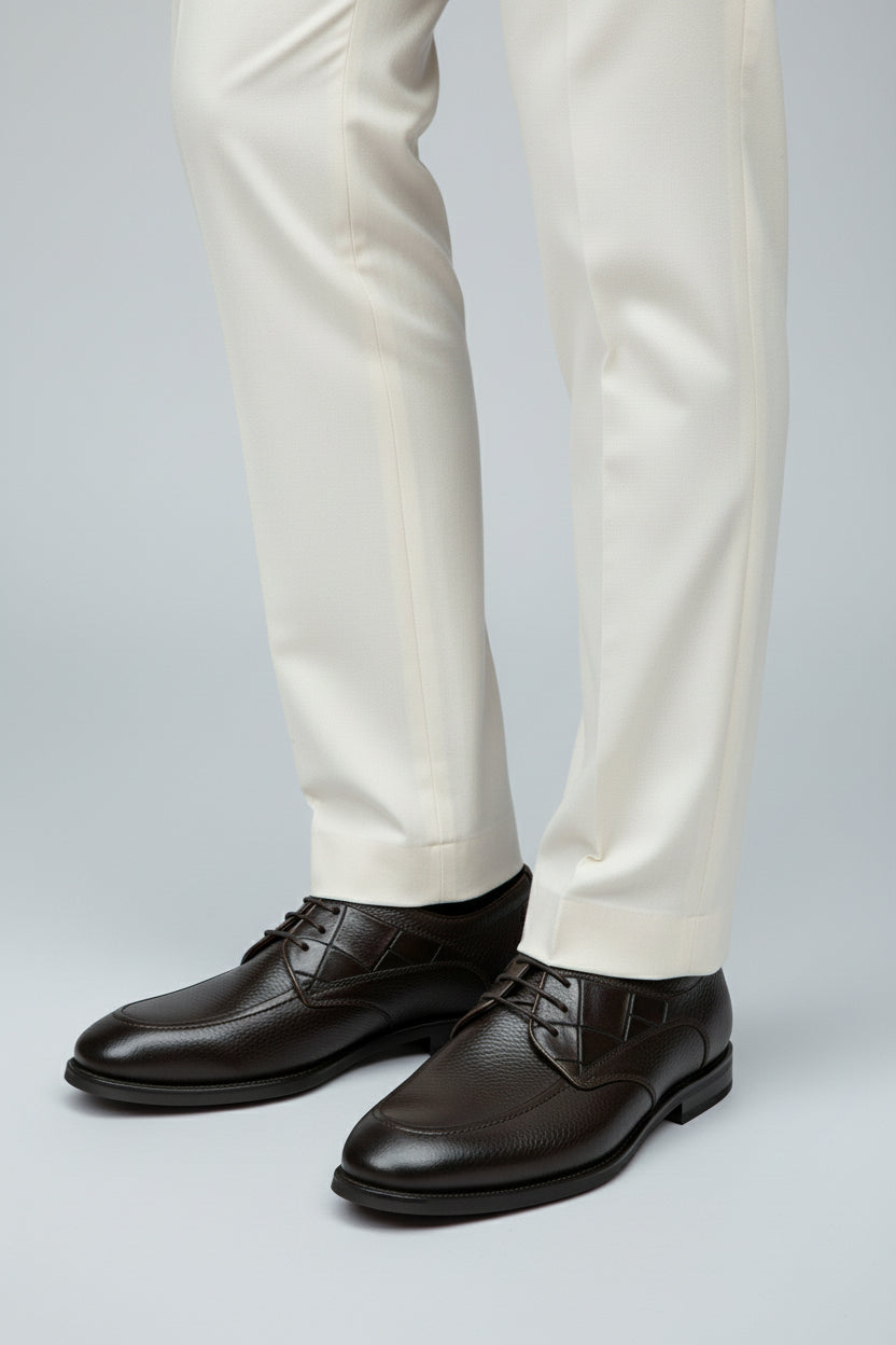 Brown leather lace-up dress shoes paired with cream tailored trousers for formal occasions.