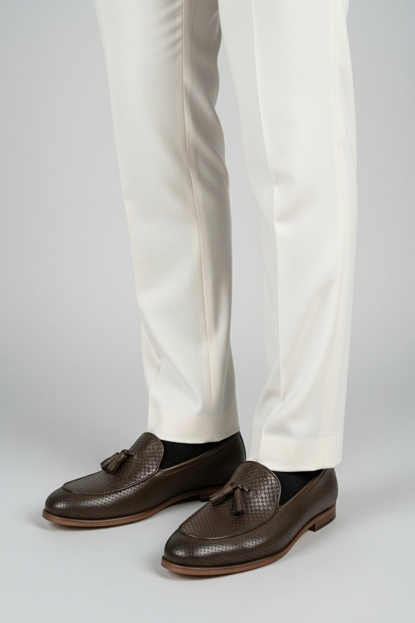 Man wearing dark brown woven leather loafers with tassels and cream tailored trousers.